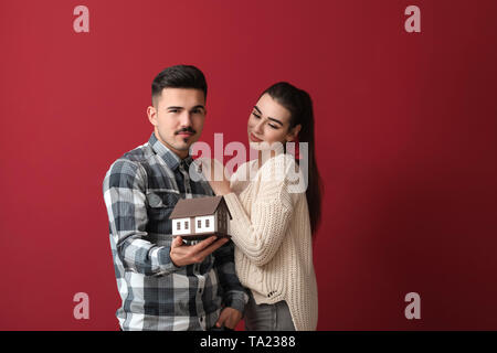 Junges Paar in der Schuld holding Abbildung von Haus auf farbigen Hintergrund Stockfoto