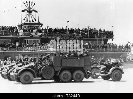 Foto eines Deutschen anti-Flugzeuge der Legion Condor (Lkw des Typs Krupp L2H143 mit einem angeschlossenen 2 cm Flak 30) während einer Siegesparade für General Francisco Franco am Flughafen Barajas, Madrid, nach der Invasion der Stadt am 28. März 1939. Im Hintergrund ist das Terminal des Flughafens mit der VIP stehen für Franco und das Symbol der faschistischen Partei Spaniens, der Falange (Pfeile und Gabeln). Stockfoto