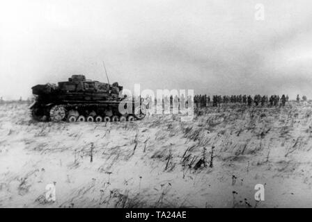 Deutsche Soldaten März über einem schneebedeckten Feld am Nordabschnitt der Ostfront. Hinter, ein Sturmgeschuetz IV. Foto der Propaganda Firma (PK): SS Kriegsberichterstatter Tschel. Stockfoto