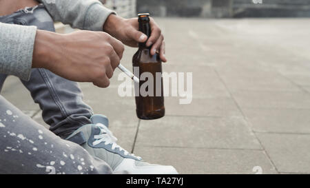 Afrikanische jugendlich Kerl allein sitzen mit Zigarette und einer Flasche Bier Stockfoto