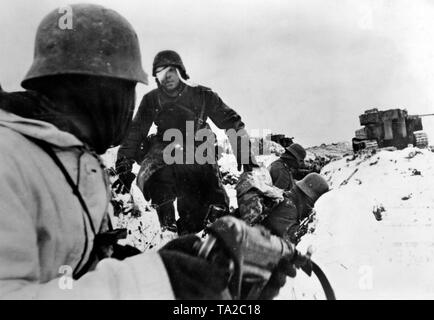 Deutsche Soldaten nehmen die Abdeckung in einem Graben von der gegnerischen Artillerie Feuer. Sie werden von einem Panzerwagen VI Tiger unterstützt. Foto der Propaganda Firma (PK): kriegsberichterstatter John. Stockfoto