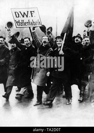 Matrosen und Arbeiter der Deutschen Waffenfabrik Marsch durch die Straßen von Berlin im November 1918. Ein Arbeitnehmer hält ein Schild mit dem Namen der Fabrik, ein Seemann hält eine rote Flagge. Stockfoto