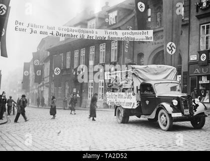 Auto der Ordnungspolizei (regelmäßige Polizei von Nazi Deutschland) mit Kundenwerbung in Telnice Tellnitz (heute). Die Stadt ist mit Hakenkreuzfahnen dekoriert. Die Sudetendeutschen halten eine Neuwahl über die Annexion des Sudetenlandes an das Deutsche Reich. Auf dem Plakat über die Straße: "Der Führer hat das Großdeutsche Reich / Ihr ja am 4. Dezember ist der letzte Hammerschlag auf das große Werk' geschmiedet. Stockfoto