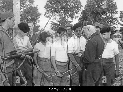 Erschöpft jungen republikanischen Gefangenen werden von spanischen Soldaten (auf der rechten Seite, eine bewaffnete falangist in einem blauen Hemd, auf der linken Seite, ein Soldat) mit einem Seil gebunden verhört. Die Soldaten (vermutlich Kommunisten) tragen helle Hemden, Hosen und baskenmützen. Stockfoto