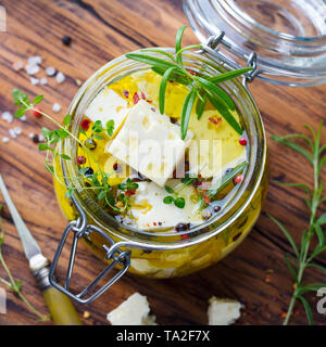 Feta Käse, mariniert in Olivenöl mit frischen Kräutern in einem Glas. Holz- Hintergrund. Ansicht von oben. Stockfoto