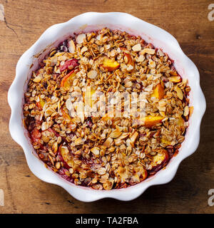 Berry, Pfirsich bröckeln, gestochen scharf in einer Auflaufform. Holz- Hintergrund. Ansicht von oben. Stockfoto