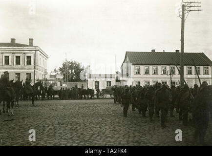 Major Josef Bischoff (2. auf seinem Pferd, Salutierte) nimmt die Salute seiner Truppen während der Invasion der Freikorps 'Eiserne Division" in Thorensberg, einem Stadtteil von Riga. Auf der rechten Seite ist ein Schild mit der Aufschrift 'Thorensberger Consum Verein'. Stockfoto