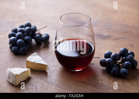 Glas Rotwein mit frischen Trauben und Käse auf dem Holztisch. Close Up. Stockfoto