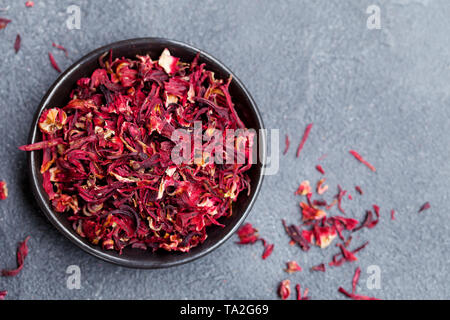 Hibiscus flower Tee in schwarz Schüssel auf grauem Stein Hintergrund. Kopieren Sie Platz. Ansicht von oben. Stockfoto