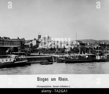 Bingen am Rhein aus dem Fluss fotografiert, im Vordergrund Pier mit Schiffen und im Hintergrund das Hotel Victoria, Burg Klopp und das Hotel Distel. Stockfoto