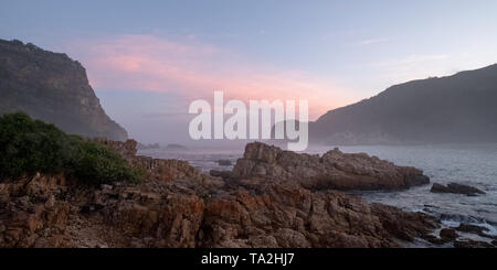 Die Staats- und Regierungschefs, Knsyna, Garden Route, Südafrika. Felsvorsprung an der Spitze der Lagune, in Nebel bei Sonnenuntergang fotografiert. Stockfoto