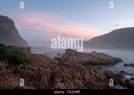 Die Staats- und Regierungschefs, Knsyna, Garden Route, Südafrika. Felsvorsprung an der Spitze der Lagune, in Nebel bei Sonnenuntergang fotografiert. Stockfoto