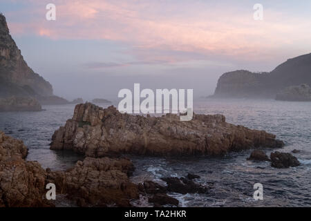 Die Staats- und Regierungschefs, Knsyna, Garden Route, Südafrika. Felsvorsprung an der Spitze der Lagune, in Nebel bei Sonnenuntergang fotografiert. Stockfoto