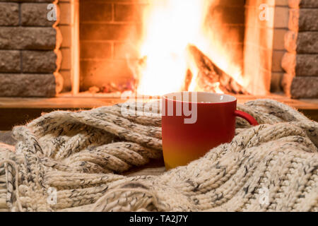 Große Tasse mit Kaffee und warmen Wolle Schal in der Nähe der gemütlichen Kamin in Country House, Winter Urlaub. Stockfoto