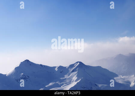 Hohe schneebedeckte Berge in Nebel und sonnendurchfluteten bewölkter Himmel im Winter Abend. Kaukasus, Georgien, Region Gudauri. Stockfoto