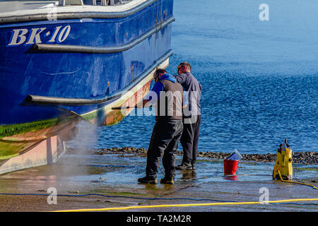 Fischer sprühen ihr Fischerboot mit einem Druckreiniger, um Algen aus dem Rumpf zu entfernen. Seahouses, Northumberland, Großbritannien. Oktober 2018. Stockfoto