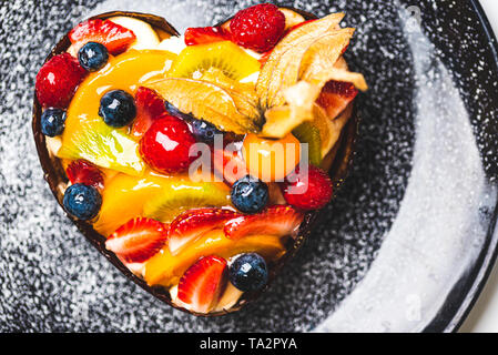 Herzförmige Frucht Biskuitteig, Obstkuchen auf schwarze Platte bestreut mit Puderzucker. Gesunde Süßwaren Hintergrund. Stockfoto