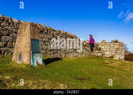 Walker neben dem trig Point auf dem Gipfel der Ros-Hügel, die Website von Ros Schloss Eisenzeit Hill fort. In der Nähe von chillingham, Northumberland, Großbritannien. November 2018. Stockfoto