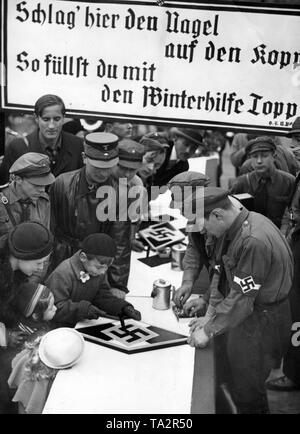 Kinder schlagen Nägel in ein Wappen der Hitlerjugend (HJ) während einer Spendenaktion für die NS-Winter Relief. Stockfoto