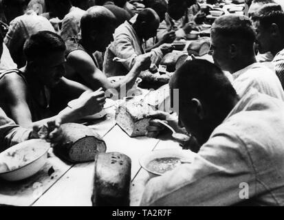 Häftlinge im KZ Dachau beim Essen. Auf der Tabelle sind mehrere Brotsorten. Dieses Foto wurde, so wie viele andere, für Propagandazwecke des NS-Regimes. Stockfoto