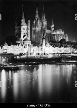 Blick auf den Kölner Rhein Ufer. Auf der Promenade die große Kirche St. Martin (links) und das Stapelhaus (rechts daneben). Im Hintergrund ist der Kölner Dom. Die Gebäude sind mit Strahlern beleuchtet. Stockfoto