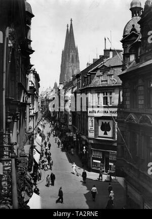 Die Hohe Straße in Köln. Passanten sind zu Fuß auf der Straße. An den Wänden der Häuser sind montiert Werbung und Beschilderung. Im Hintergrund über den Dächern, die Türme der Kathedrale. Undatiertes Foto. Vor dem Krieg, da die Gebäude nicht beschädigt sind. Stockfoto