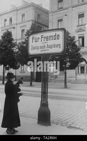 Eine Frau mit einem Hund in ihre Arme steht vor einem Schild mit den Worten "für Ausländer, der Umzug nach Augsburg ist verboten." Stockfoto