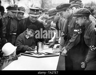 Kinder schlagen Nägel in ein Wappen der Hitlerjugend (HJ) während einer Spendenaktion für die NS-Winter Relief. Stockfoto