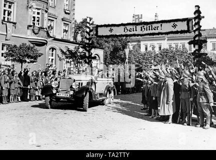 Adolf Hitler (vorne im Auto links) bei einem Besuch in Jaegerndorf (heute Krnov) am 7. Oktober 1938, während der Besetzung des Sudetenlandes durch Deutschland. Die Bevölkerung erhält ihm, indem er ihm den Hitlergruß. Über der Straße, ein Banner mit der Aufschrift: "Heil Hitler!" Stockfoto