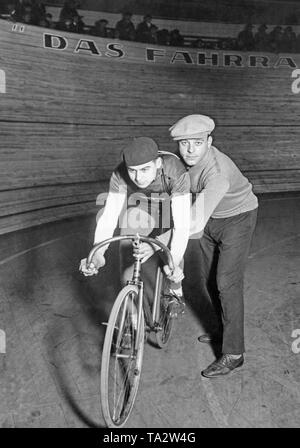 Eine spur Radfahrer und sein Assistent, der ihn unterstützt, posieren für ein Foto vor dem Radweg im Berliner Sportpalast vor Beginn der Sechs Tage Rennen. Stockfoto