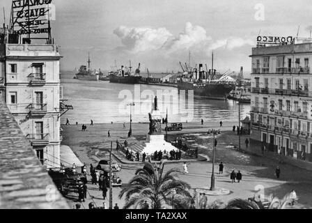 Blick auf die Plaza de San Juan de Dios in Cadiz, Andalusien, Spanien am 17. Februar 1937. Im Hintergrund, das Dock von Cadiz. Am Ende des Kais, die Spanische Cruiser 'Candrias' achor, der modernsten Kriegsschiff von Spanien zu dieser Zeit. In den Vordergrund, der Hauptplatz von Cadiz mit dem Denkmal des ehemaligen Ministerpräsidenten von Spanien, segismundo Moret y Prendergast (1833-1913). Rechts am Gebäude, die Symbole (Gabel und Pfeile) der Falange Espanola, die faschistische Partei Spaniens. Es ist vermutlich der Sitz der Falange in Cadiz. Stockfoto