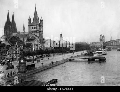 Blick auf die Rheinpromenade und den Fischmarkt in Köln am 2.10.1935. Rechts, dem Rhein mit Schiffen und Liegeplätze. Rechts im Hintergrund die Hohenzollernbrücke in seiner ursprünglichen Form mit Türmen und Portale. Auf der linken Seite im Hintergrund die Türme der Kathedrale. Vor, dass die große Kirche St. Martin. Direkt davor, den Turm der Stapelhaus. An der Promenade sind Fußgänger und Autos. Stockfoto