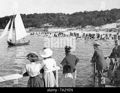 Urlauber Blick auf einem Segelboot vom Steg aus. Am Strand sind Liegestühle, dass die Badegäste vor der Sonne schützen. Stockfoto