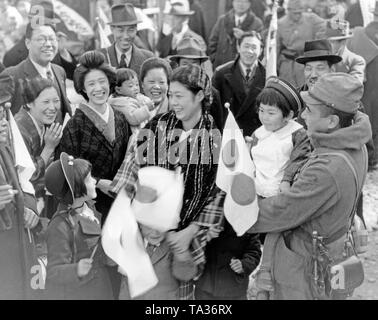 Eine Gruppe von Menschen nehmen Abschied von einem japanischen Soldaten, der in China an der Vorderseite während des Zweiten Japanese-Chinese Krieg geschickt wird. Sie halten japanische Flaggen in den Händen und Lachen. Stockfoto
