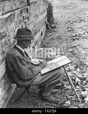 Maler beim Malen in der verwüsteten München, um ihn herum Schutt. Aus der Not heraus, er verwendet eine behelfsmäßige Lösung als Inhaber. Stockfoto