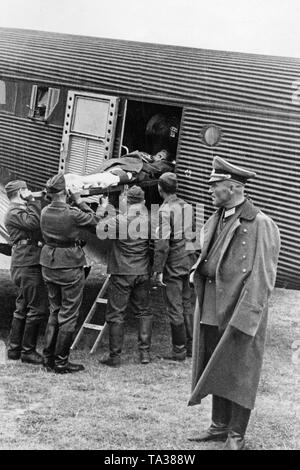 Foto eines Verwundeten deutschen Soldaten der Legion Condor beim Entladen in Deutschland. Soldaten der Luftwaffe (US Air Force) tragen die verletzten Soldaten auf einer Bahre aus der Junkers Ju 52 zu einem Krankenwagen. Im Vordergrund, ein Offizier in der Uniform der Wehrmacht. Stockfoto