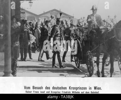 Kronprinz Wilhelm von Preußen (Mitte des Bildes in die Kamera schaut) bei einem Besuch in Wien. An der Station, die er von Kaiser Franz Josef von Habsburg begrüßt wird (hinter dem Schlitten links), und steigt mit ihm in einen wartenden Bus. Stockfoto