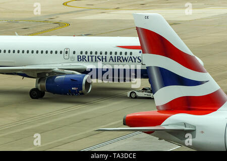 Der Flughafen London Gatwick, ENGLAND - April 2019: Schwanzflosse eines British Airways Jet am Flughafen Gatwick mit einem anderen BA Jet im Hintergrund. Stockfoto