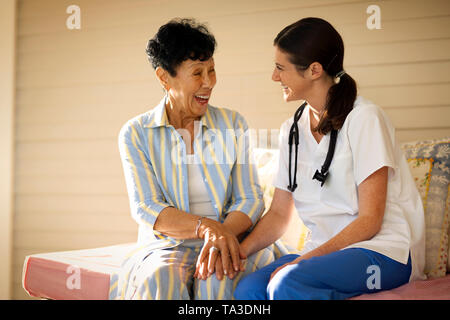 Junge weibliche Krankenschwester sitzen mit einen älteren Patienten auf Ihrer Veranda, Stockfoto