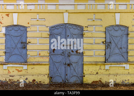 Alte gelbe flache Wand mit Eisen geschmiedet Türen und geschlossenen Fensterläden Stockfoto