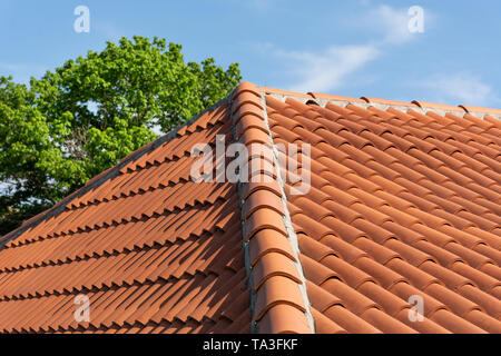 Orange Dachziegel Muster über Blau und trübe frühlingshimmel Tag und grünen Bäumen im Hintergrund. Das Dach auf modernen Gebäude. Nahaufnahme Stockfoto
