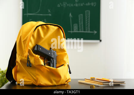 Rucksack mit Pistole auf Tisch im Klassenzimmer. Keine Gewehre in der Schule Stockfoto