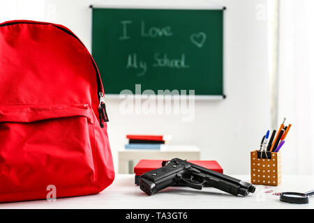 Rucksack, Pistole und Schreibwaren auf Tisch im Klassenzimmer. Keine Gewehre in der Schule Stockfoto