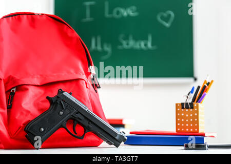 Rucksack, Pistole und Schreibwaren auf Tisch im Klassenzimmer. Keine Gewehre in der Schule Stockfoto