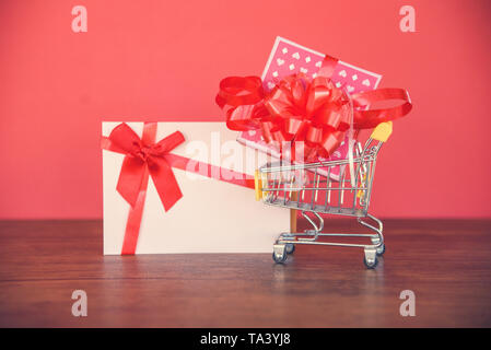 Valentines Tag einkaufen und Geschenkkarte Geschenkverpackung/rosa Geschenk Box mit roter Schleife auf Warenkorb Frohe Weihnachten Frohes neues Jahr oder Va Stockfoto