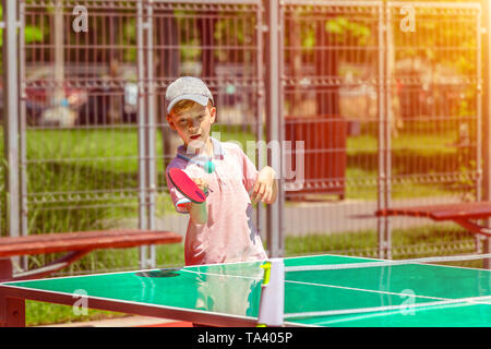 Süßer kleiner Junge spielt Tischtennis in park-Aktivität im Freien im Sport Boden mit lachenden Kind Spaß haben, Lernen und Üben von Ping pong Stockfoto