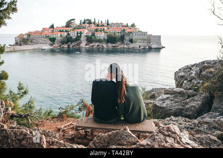 Ein junges Paar von Touristen bewundert die schöne Aussicht auf das Meer und die Insel Sveti Stefan in Montenegro. Stockfoto