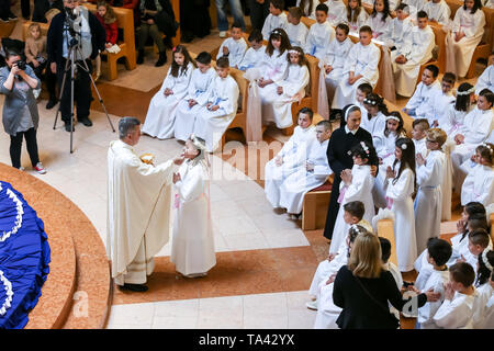 Zagreb, Kroatien - 5. Mai 2019: Der Priester gibt Erstkommunion für die Kinder in weißen Kleidern während der Kommunion in der Kirche von Alle gekleidet Stockfoto