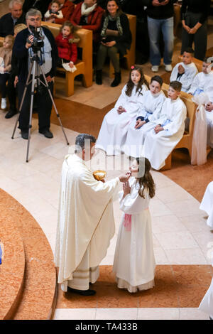 Zagreb, Kroatien - 5. Mai 2019: Der Priester gibt Erstkommunion für die Kinder in weißen Kleidern während der Kommunion in der Kirche von Alle gekleidet Stockfoto