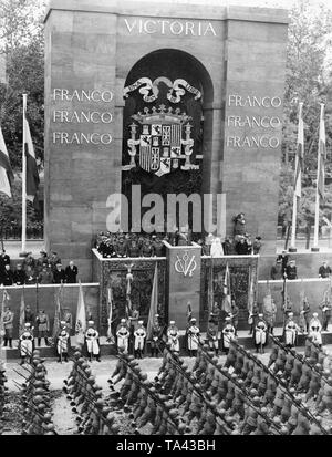 Foto der Caudillo General Francisco Francos während der siegesparade in Paseo della Castellana, Madrid, am 19. Mai 1939. Franco ist Salutierte auf der Tribüne, die durch hochrangige Offiziere und Würdenträger umgeben. Eine Einheit der italienischen Soldaten aus dem freiwilligen Corpo Truppe Volontarie marschiert durch den Triumphbogen. Stockfoto